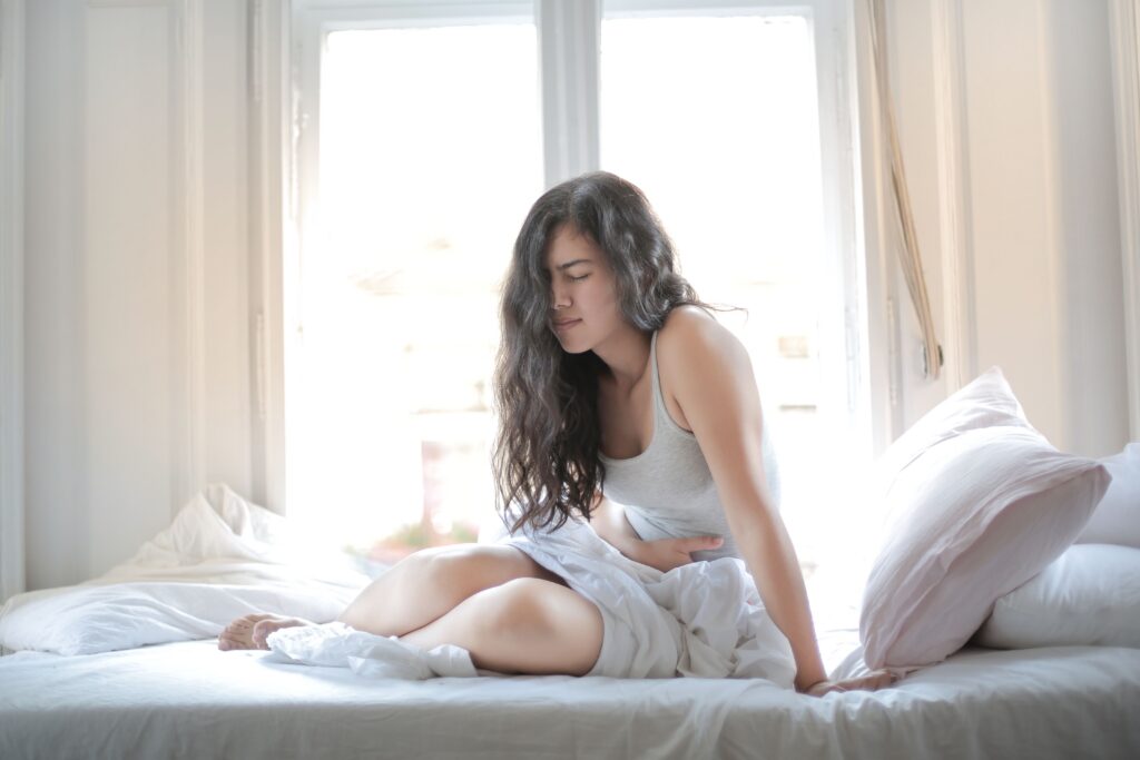 Woman sitting on a bed with lower abdominal discomfort, representing chronic pelvic pain that may be linked to pelvic venous disorder